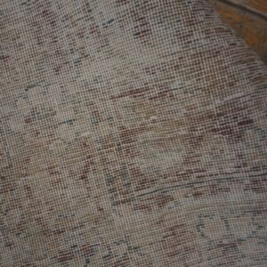 Close-up view of a low-pile beige rug with distressed brown pattern on wood flooring.