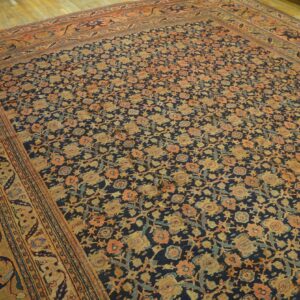 Low-pile rug features dense orange and gold floral motifs on a dark blue background over hardwood.