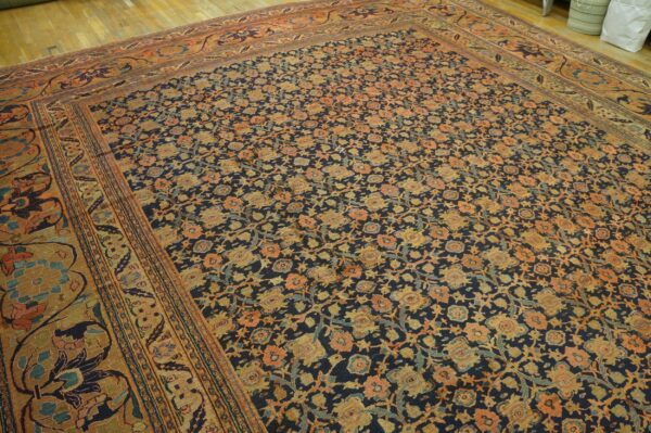 Low-pile rug features dense orange and gold floral motifs on a dark blue background over hardwood.