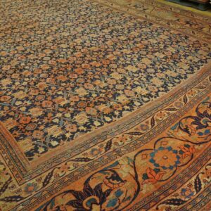 Navy and orange traditional rug featuring dense floral motifs and ornate borders on wood flooring.