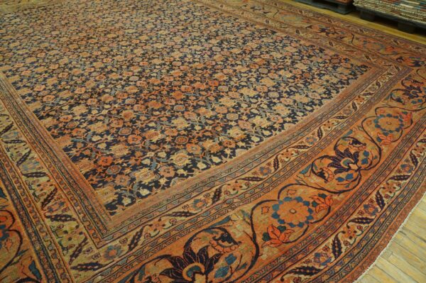 Navy and orange traditional rug featuring dense floral motifs and ornate borders on wood flooring.