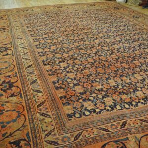 Large low-pile rug featuring a dense navy and orange floral pattern displayed on a light wood floor.
