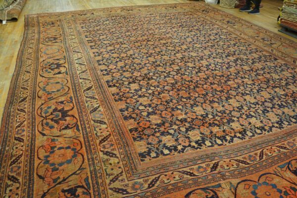 Large low-pile rug featuring a dense navy and orange floral pattern displayed on a light wood floor.