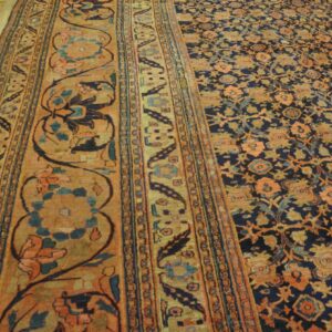 Dark blue and orange ornate rug on light wood floor showing a patterned border and central field.