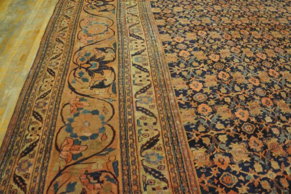 Dark blue and orange ornate rug on light wood floor showing a patterned border and central field.