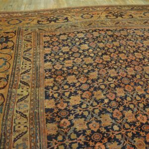 Dark blue rug with dense orange and gold floral patterns and a wide ochre border on wood floors.