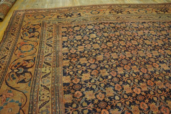 Dark blue rug with dense orange and gold floral patterns and a wide ochre border on wood floors.