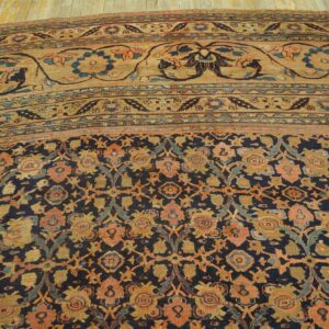 Ornate floral rug with a navy field, a wide tan border, and faded orange and gold motifs.