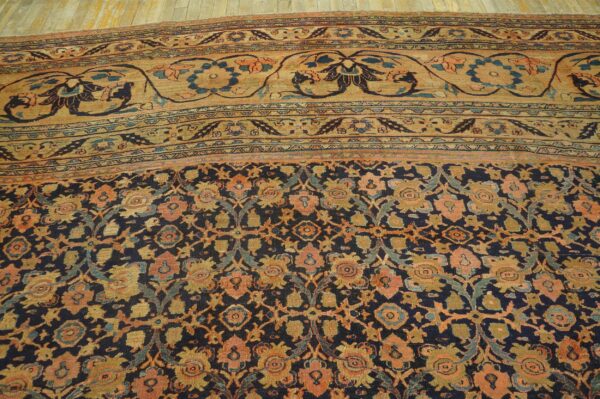 Ornate floral rug with a navy field, a wide tan border, and faded orange and gold motifs.