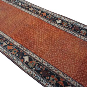 Rust colored runner rug with a repeating lattice pattern and geometric dark blue guard borders.