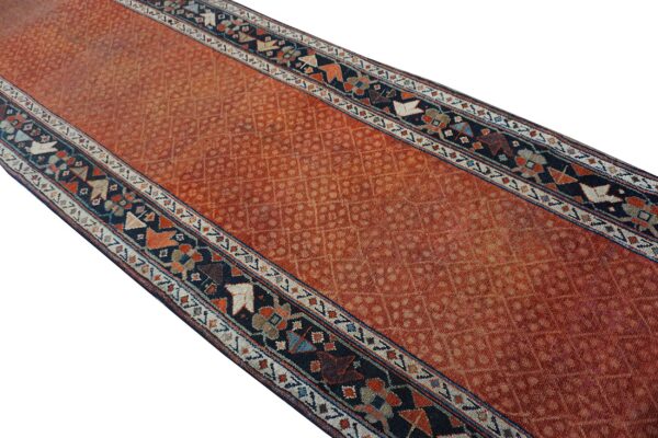 Rust colored runner rug with a repeating lattice pattern and geometric dark blue guard borders.