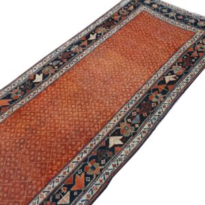 Long runner rug featuring an all-over diamond motif on a faded terracotta field and a dark geometric border.