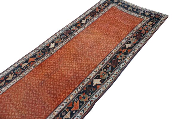 Long runner rug featuring an all-over diamond motif on a faded terracotta field and a dark geometric border.