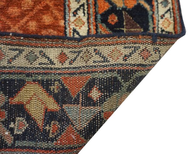 Thick orange pile contrasts with the tightly woven beige, navy, and rust geometric pattern on the rug's reverse.