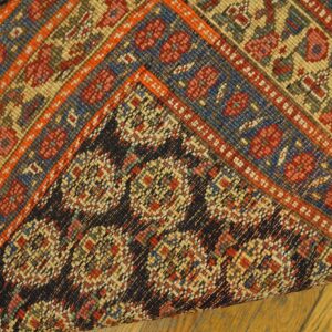 Multicolor geometric rug detail shows the woven face and dark, tightly patterned backing on a wood floor.