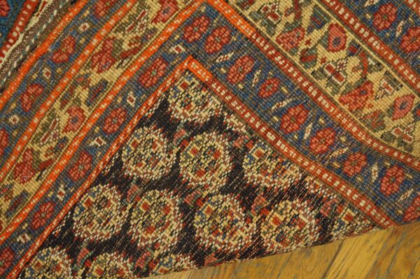 Multicolor geometric rug detail shows the woven face and dark, tightly patterned backing on a wood floor.