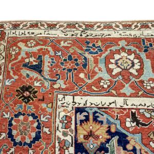 Detailed view of a low-pile rug in rust red, navy, and cream, featuring detailed floral motifs and script in the border.