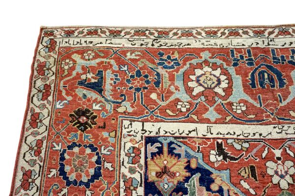 Detailed view of a low-pile rug in rust red, navy, and cream, featuring detailed floral motifs and script in the border.