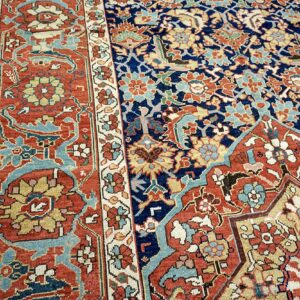 Detailed view of a traditional rug showing a navy blue center and a rust red border with floral motifs.