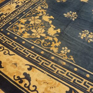 A blue rug featuring golden floral and fretwork borders covers light brown wood plank flooring.