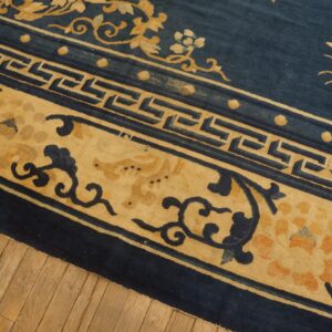 Navy blue rug with wide tan borders detailed with florals and a geometric fret pattern over wood floors.