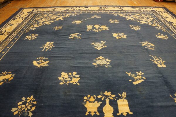 Navy blue rug with scattered pale yellow floral motifs and a detailed geometric border on wood flooring.