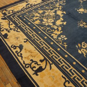 Deep blue rug with golden yellow floral and fret borders over wide, aged wood flooring.