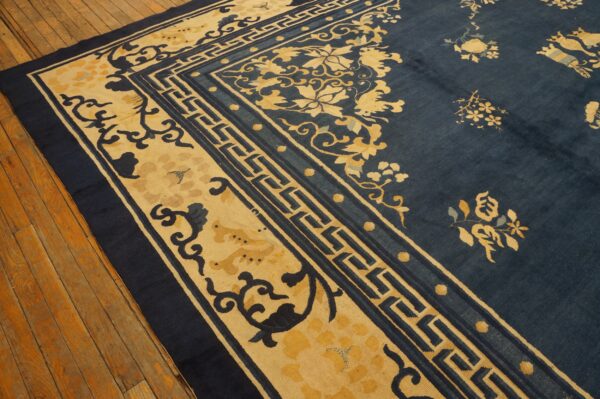Deep blue rug with golden yellow floral and fret borders over wide, aged wood flooring.
