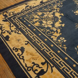 Navy blue rug with intricate gold floral patterns and geometric fretwork borders on distressed wood flooring.
