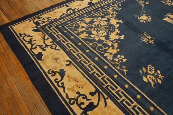 Navy blue rug with intricate gold floral patterns and geometric fretwork borders on distressed wood flooring.