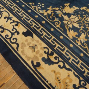 Navy blue rug with tan floral and key border patterns shown on light hardwood flooring.