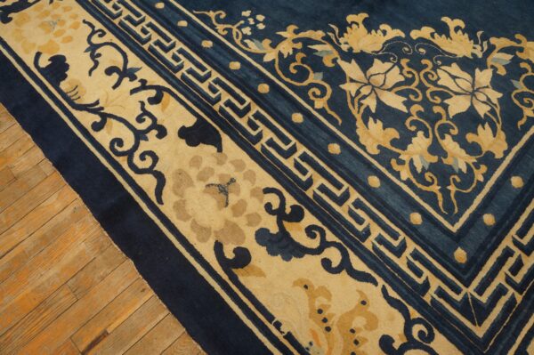 Navy blue rug with tan floral and key border patterns shown on light hardwood flooring.