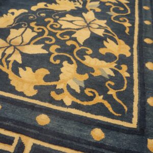 Detailed view of a low-pile rug showing indigo field, gold floral vines, and a fretwork geometric border.