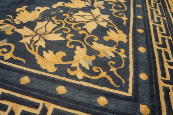 Detailed view of a low-pile rug showing indigo field, gold floral vines, and a fretwork geometric border.