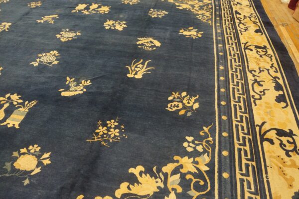 Dark blue rug featuring scattered yellow and blue floral motifs and a wide patterned yellow border on wood floor.