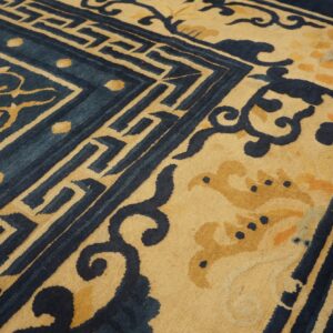 Deep indigo and gold rug close-up showing intricate scrolling vines and geometric border patterns.