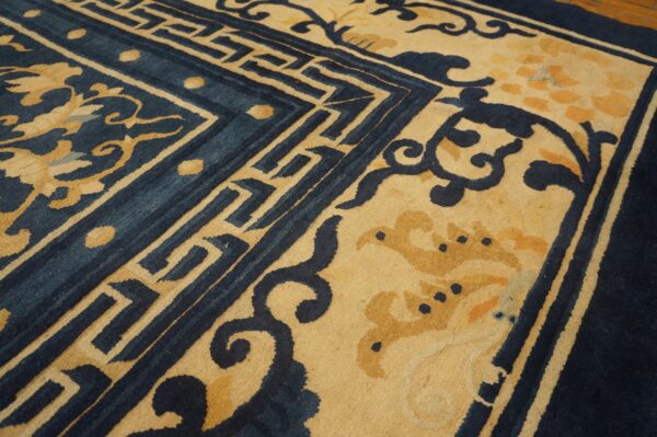 Deep indigo and gold rug close-up showing intricate scrolling vines and geometric border patterns.