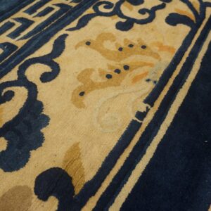 Textured navy blue and cream rug featuring scroll and geometric patterns on a distressed wood floor.