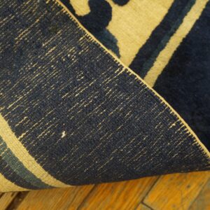 Navy and yellow rug edge curled over a distressed yellow-orange wood floor, showing the woven backing.