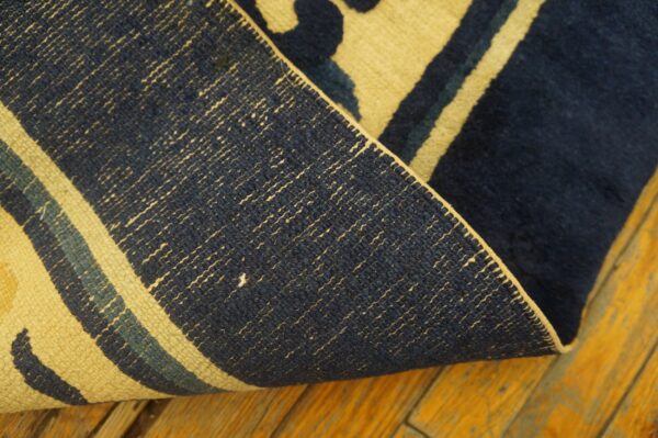 Navy and yellow rug edge curled over a distressed yellow-orange wood floor, showing the woven backing.