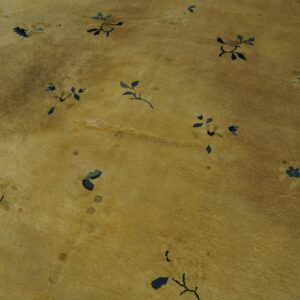 Golden-yellow low pile rug with scattered navy and light blue floral designs, showing heavy wear and discoloration.