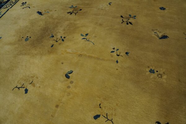 Golden-yellow low pile rug with scattered navy and light blue floral designs, showing heavy wear and discoloration.