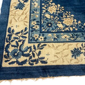Detailed view of a deep blue rug corner with beige and lighter blue floral motifs in the borders.