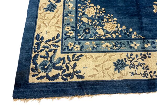 Detailed view of a deep blue rug corner with beige and lighter blue floral motifs in the borders.