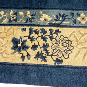 Plush pile rug detail showing blue, teal, and tan floral borders against a dark blue ground.
