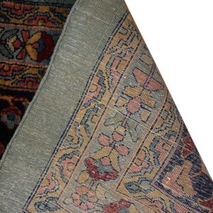 A dark red and gold patterned rug corner is lifted to show the light green woven backing.