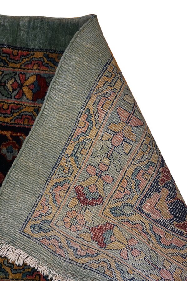 A dark red and gold patterned rug corner is lifted to show the light green woven backing.