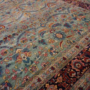 Ornate sage rug with a high pile, featuring red, gold, and blue traditional floral patterns and a navy border.