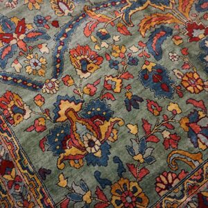 The rug shows dense traditional patterns in deep blue, rust, and gold against a muted green pile.