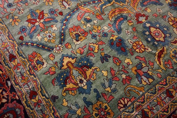 The rug shows dense traditional patterns in deep blue, rust, and gold against a muted green pile.